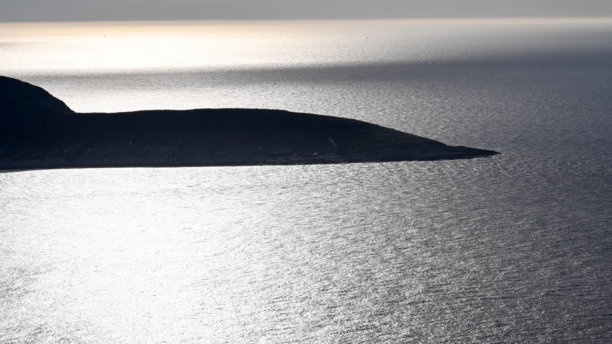 Silueta výbežku Knivskjellodden počas polnočného slnka, kedy slnečné lúče odrážajú svetlo od oceánu.
        