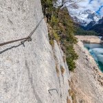 Foto 9: Pohľad zo skalnej steny ferraty s istiacim lanom a výhľadom na roztápajúce sa jazero s nízkou hladinou vody a Dachstein
