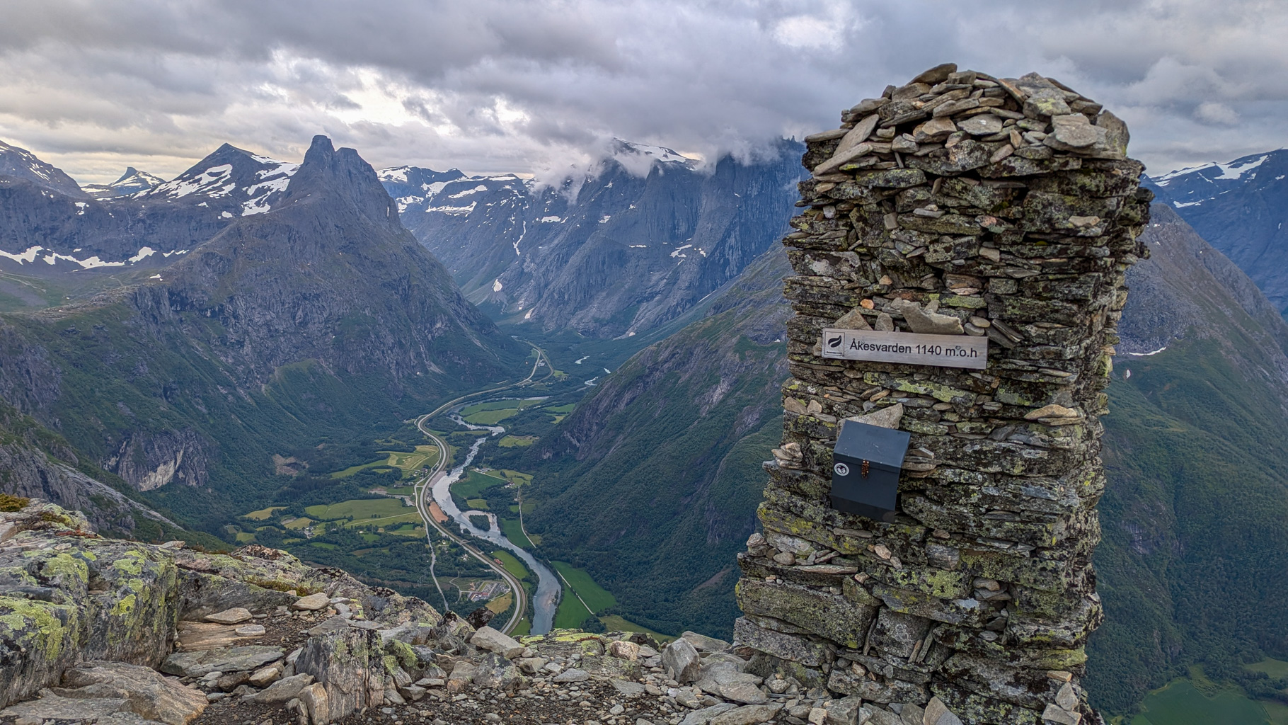 Výhľad z vrcholu Åkesvarden (1140 m), jedného z vrcholov hrebeňa, na údolie rieky Rauma a Trollstigen v
            diaľke. Mohyla na vrchole je typickým cieľom túry.
        