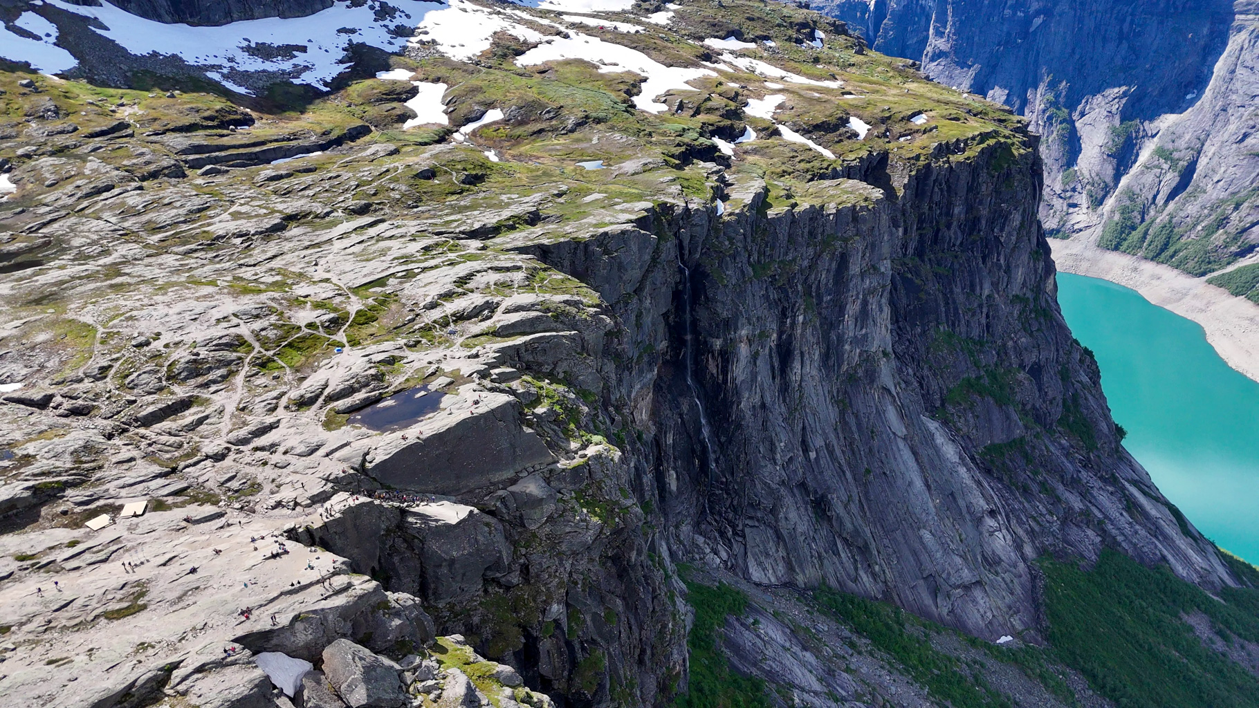 Letecký pohľad na Trolltungu a čakajúcich turistov s vodopádom v pozadí.