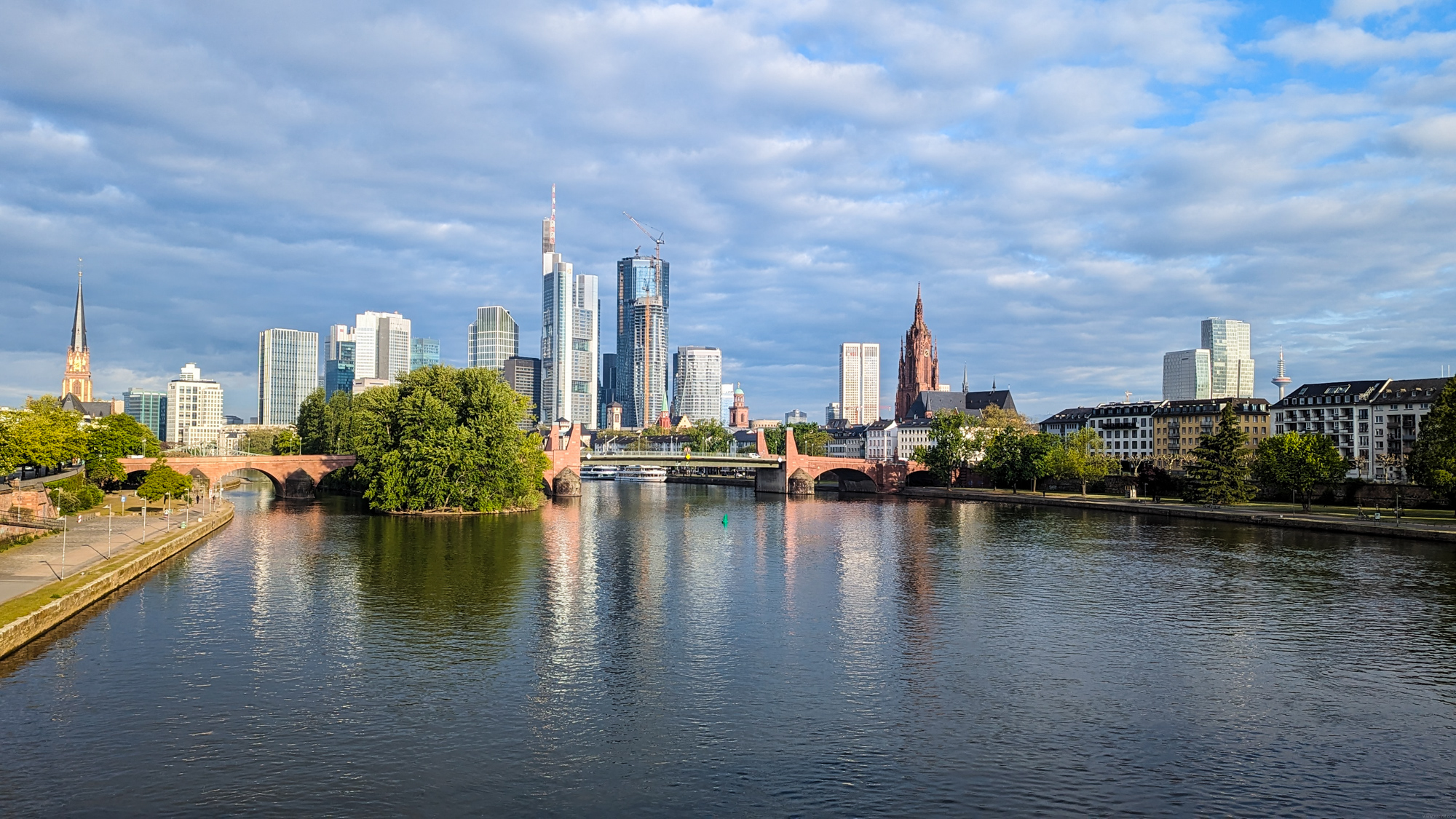 Panoráma Frankfurtu s riekou Mohan (Main), starým mostom Alte Brücke, modernými výškovými budovami a frankfurtským dómom vpravo.