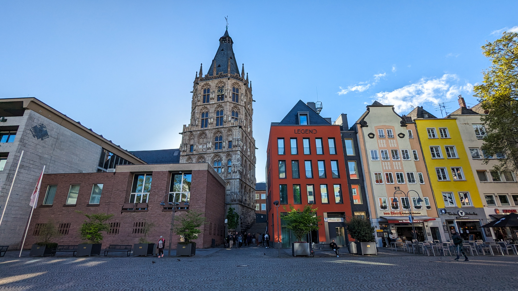 Pohľad na budovu starej radnice (Kölner Rathaus) s výraznou gotickou vežou, obklopenú farebnými mestskými domami.
