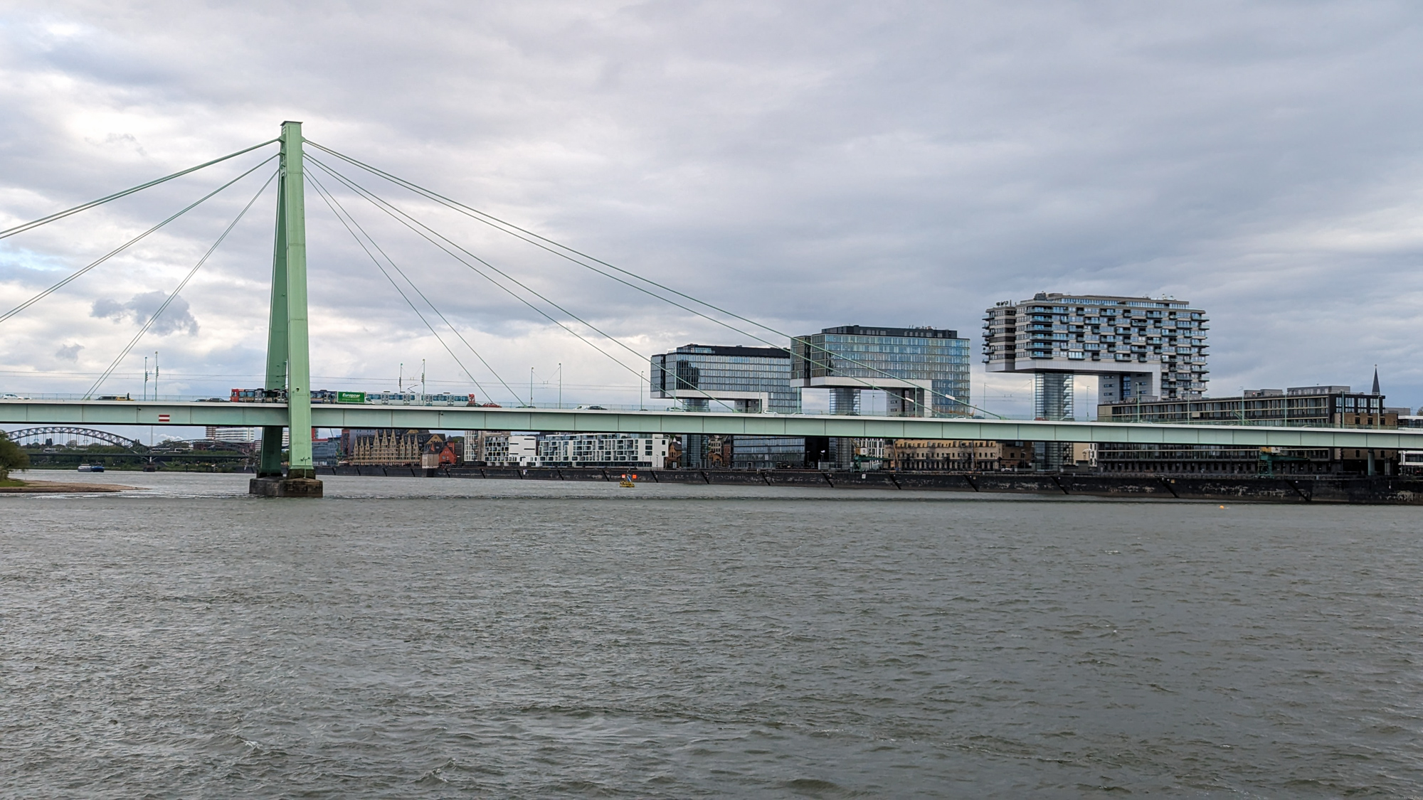 Záber na zelený most Südbrücke ponad rieku Rýn s modernou architektúrou v pozadí.