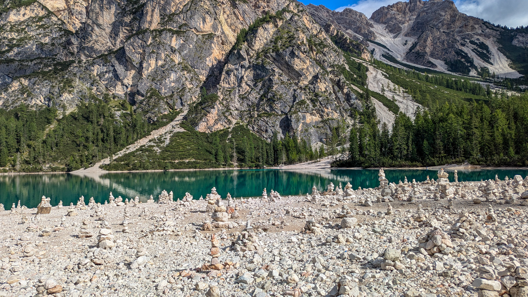 Kamenné vežičky na brehu Lago di Braies vytvorené turistami ako symboly želaní či vďaky – v pozadí steny Dolomitov.