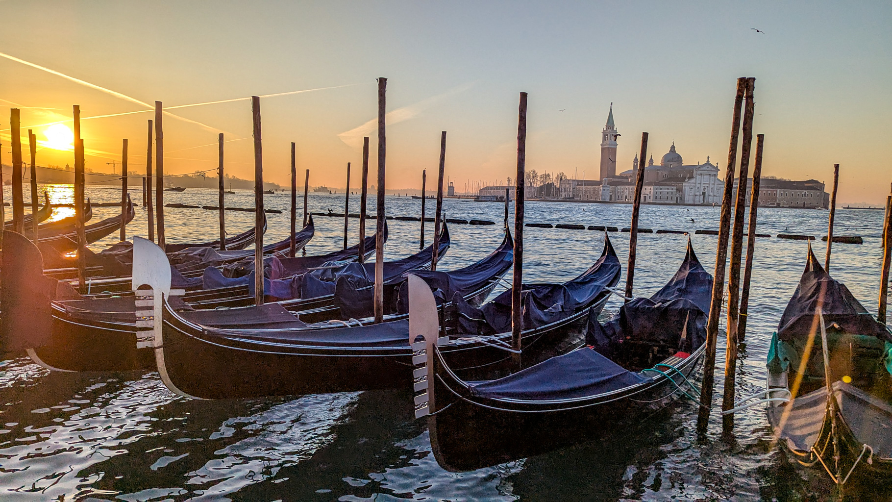 Gondoly zakotvené na lagúne pred východom slnka s pohľadom na ostrov San Giorgio Maggiore v Benátkach.
        